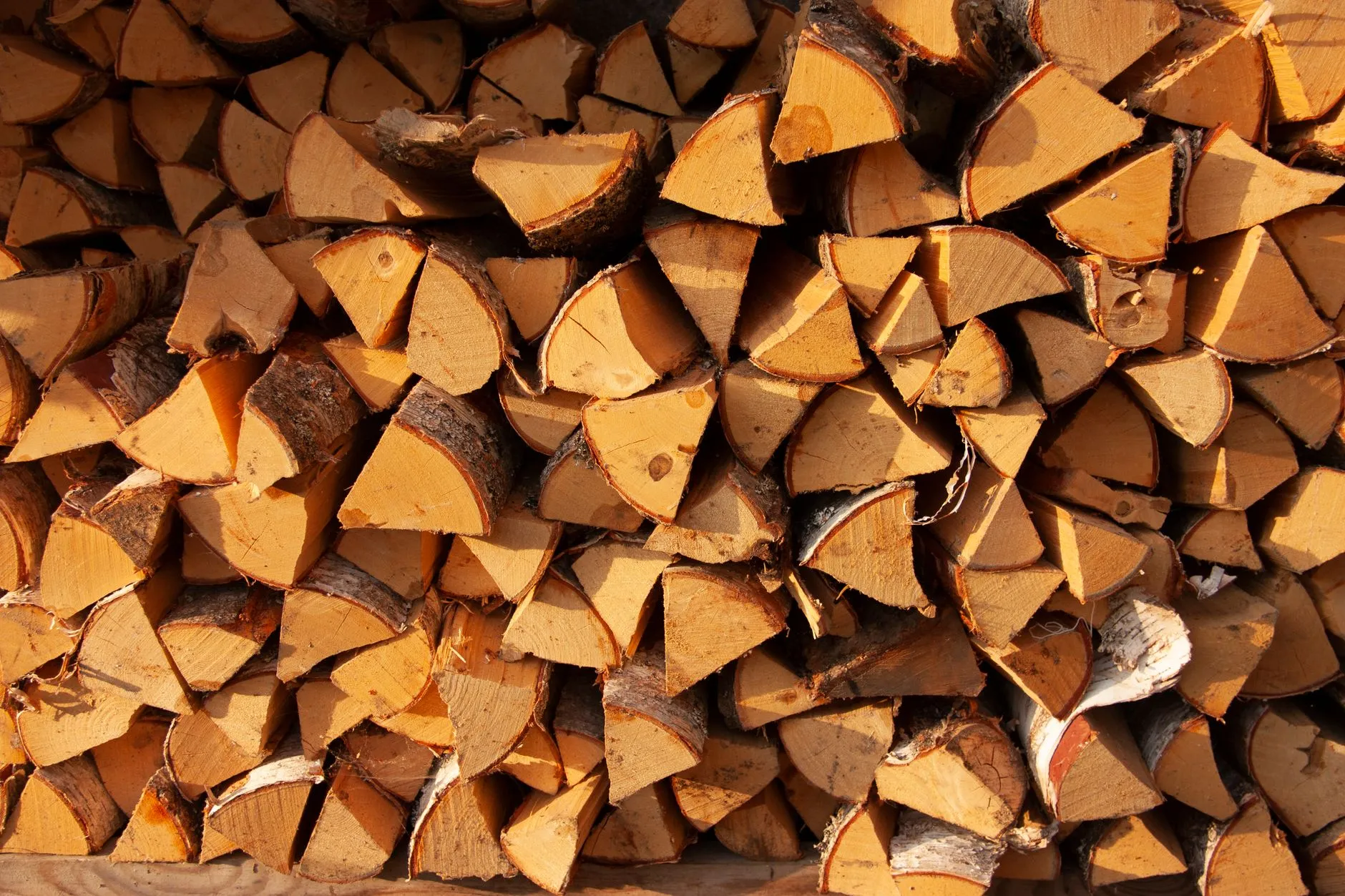 Close-up of a neatly stacked pile of split firewood logs in warm sunlight